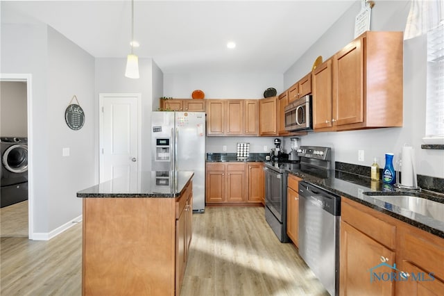 kitchen featuring pendant lighting, light hardwood / wood-style flooring, appliances with stainless steel finishes, washer / dryer, and dark stone counters