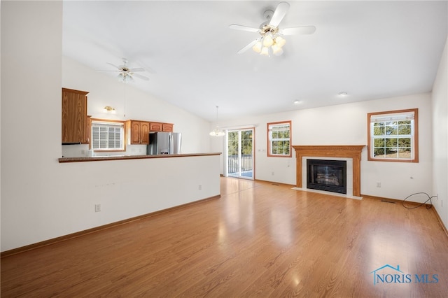 unfurnished living room with ceiling fan with notable chandelier, vaulted ceiling, and light wood-type flooring