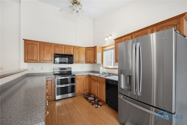 kitchen with a towering ceiling, black appliances, sink, ceiling fan, and light hardwood / wood-style floors