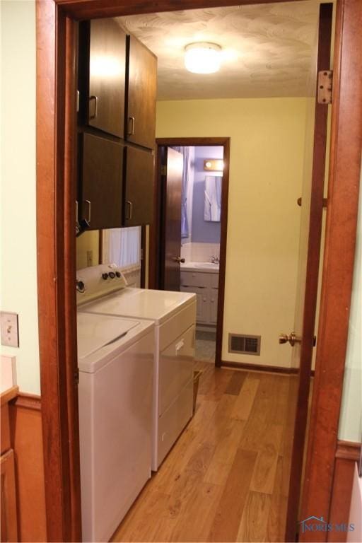 clothes washing area featuring independent washer and dryer, cabinets, sink, and light hardwood / wood-style flooring