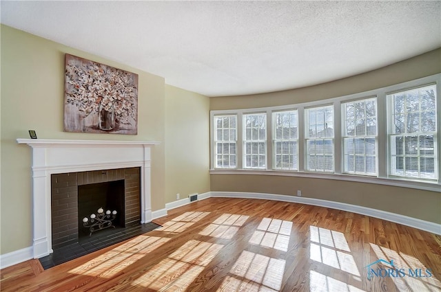 unfurnished living room with hardwood / wood-style floors, a brick fireplace, and a textured ceiling