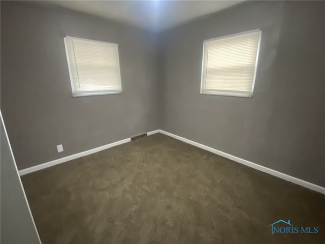 empty room featuring a healthy amount of sunlight and dark colored carpet