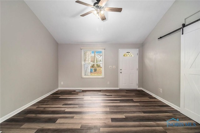 foyer entrance featuring ceiling fan, a barn door, dark hardwood / wood-style flooring, and vaulted ceiling