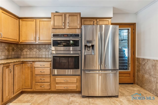 kitchen featuring light tile patterned flooring, appliances with stainless steel finishes, tile walls, and light stone counters