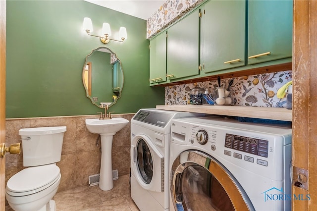 laundry room with tile walls, light tile patterned floors, washer and clothes dryer, and sink