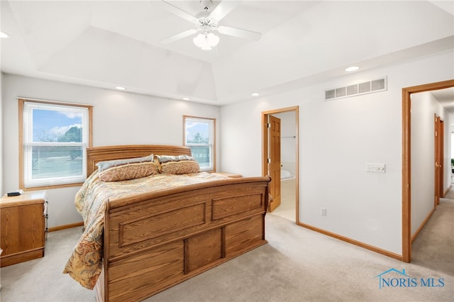 bedroom featuring connected bathroom, light colored carpet, ceiling fan, and a tray ceiling