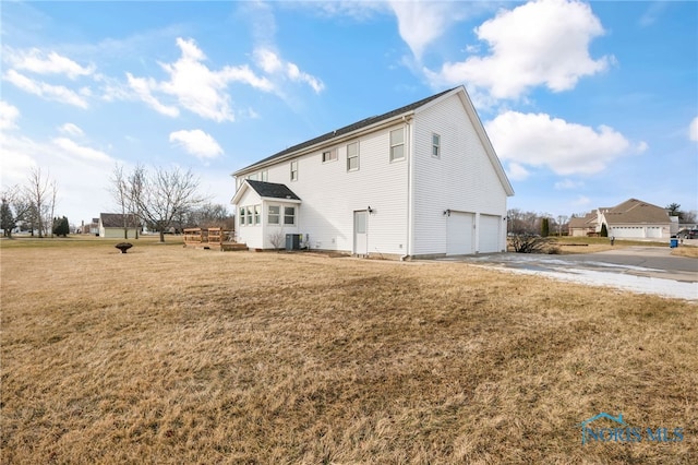 rear view of property featuring a garage, a lawn, and central air condition unit