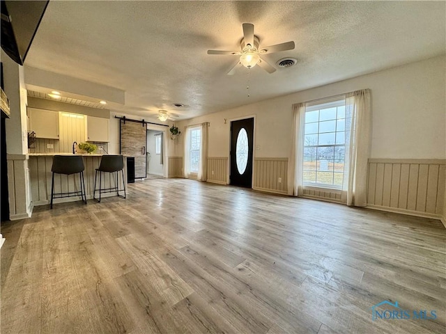 unfurnished living room with plenty of natural light, a barn door, and light wood-type flooring