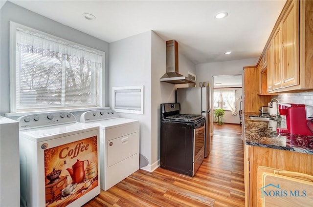 kitchen with light wood-type flooring, wall chimney range hood, light brown cabinetry, gas range, and decorative backsplash