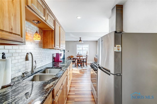 kitchen featuring light wood-type flooring, hanging light fixtures, sink, dark stone counters, and appliances with stainless steel finishes