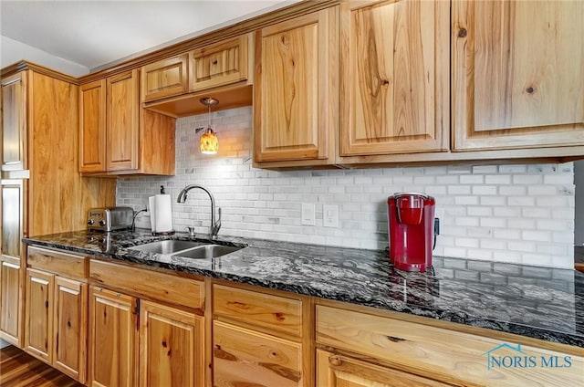 kitchen with sink, tasteful backsplash, dark stone counters, and pendant lighting