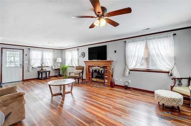 living room with ceiling fan, light hardwood / wood-style floors, crown molding, and a tiled fireplace