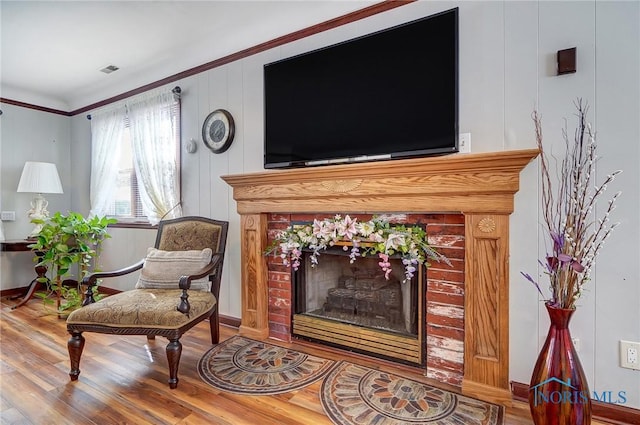 sitting room with ornamental molding, a tiled fireplace, and hardwood / wood-style floors