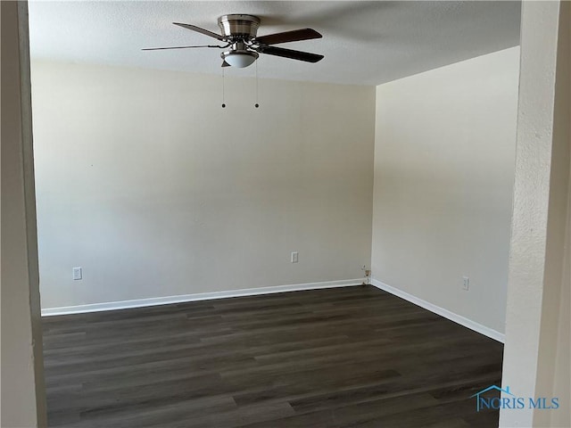 spare room with dark wood-type flooring, ceiling fan, and baseboards