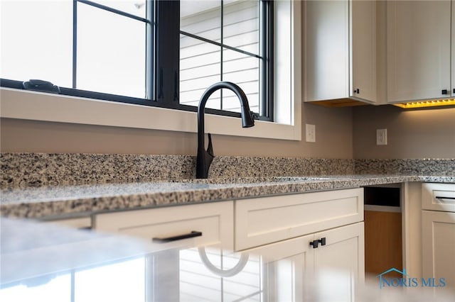 interior details featuring sink, white cabinets, and light stone counters