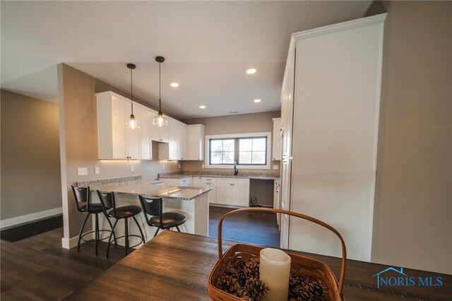 kitchen featuring light stone counters, white cabinets, dark hardwood / wood-style flooring, decorative light fixtures, and kitchen peninsula