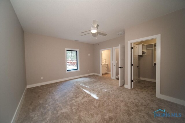 unfurnished bedroom with ensuite bathroom, a walk in closet, carpet flooring, a closet, and ceiling fan