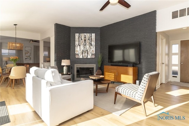 living room featuring ceiling fan, a fireplace, and light wood-type flooring