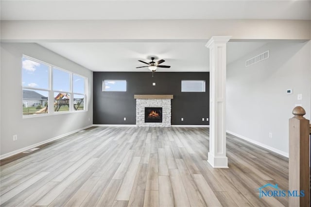 unfurnished living room with ornate columns, ceiling fan, a stone fireplace, and light wood-type flooring