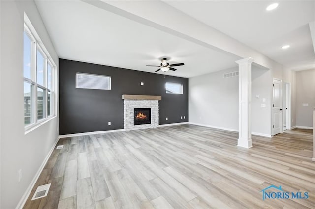 unfurnished living room with decorative columns, a healthy amount of sunlight, a fireplace, and light wood-type flooring