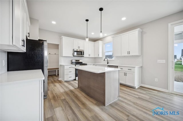 kitchen with pendant lighting, stainless steel appliances, a kitchen island, and white cabinets