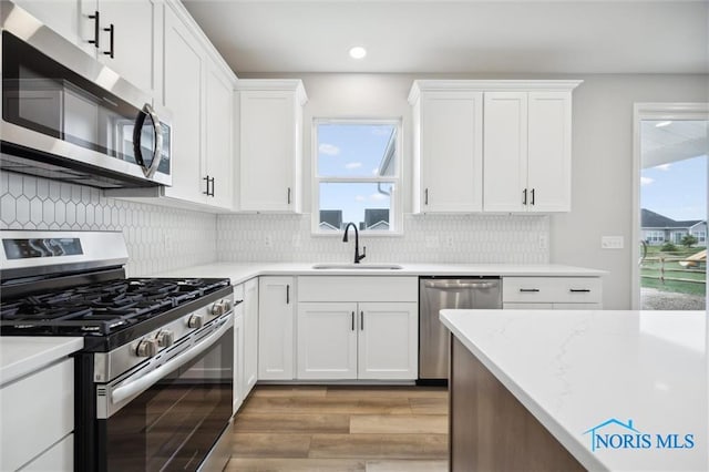 kitchen with sink, white cabinetry, light hardwood / wood-style flooring, appliances with stainless steel finishes, and decorative backsplash