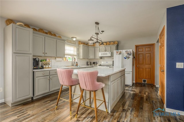 kitchen featuring sink, gray cabinetry, a kitchen island, pendant lighting, and white appliances