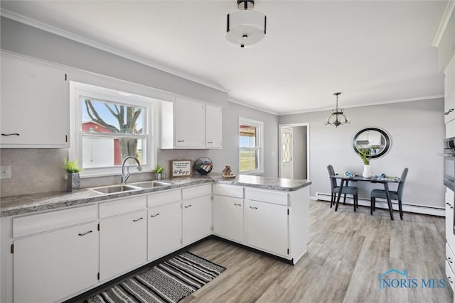 kitchen with white cabinetry, a baseboard heating unit, sink, and decorative light fixtures