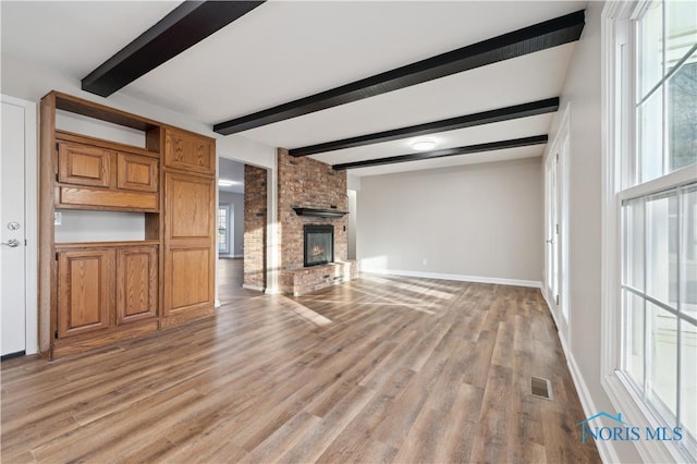 unfurnished living room with beamed ceiling, a brick fireplace, and light hardwood / wood-style flooring