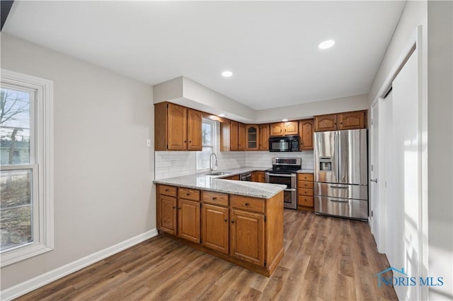 kitchen featuring sink, backsplash, hardwood / wood-style floors, stainless steel appliances, and light stone counters