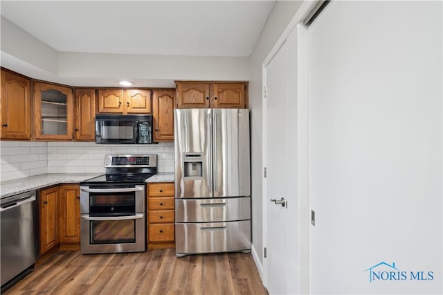 kitchen with stainless steel appliances, light stone countertops, hardwood / wood-style flooring, and backsplash