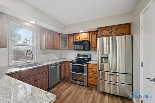 kitchen with sink, decorative backsplash, stainless steel appliances, light stone countertops, and dark wood-type flooring