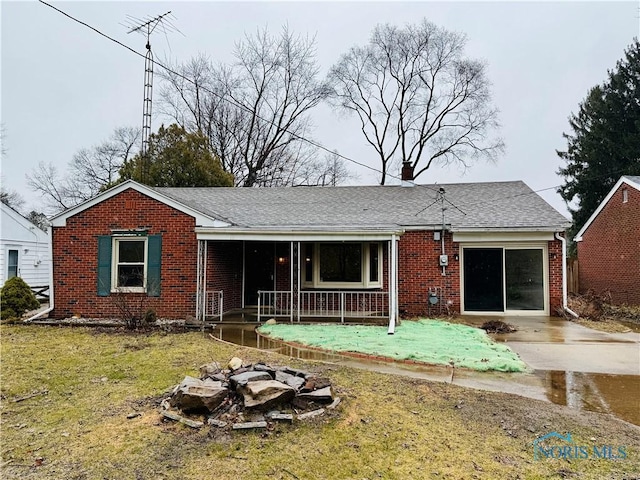 view of front facade featuring covered porch, brick siding, a shingled roof, concrete driveway, and a front yard