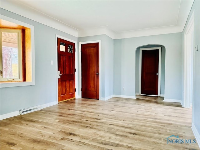 foyer featuring light wood-type flooring, arched walkways, visible vents, and baseboards