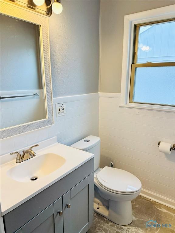 bathroom with vanity, toilet, and tile walls