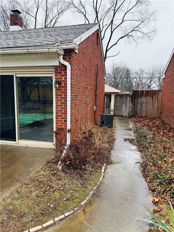 view of property exterior with brick siding, a chimney, a shingled roof, fence, and cooling unit