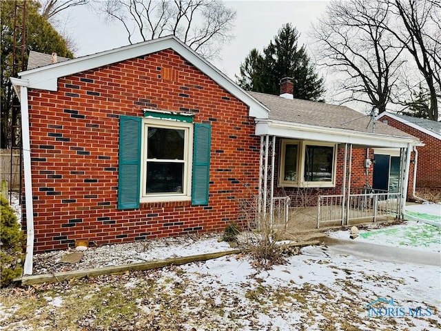 view of front of property featuring brick siding, a chimney, and roof with shingles