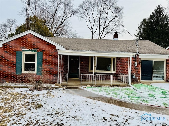 ranch-style home featuring covered porch, roof with shingles, brick siding, and a chimney