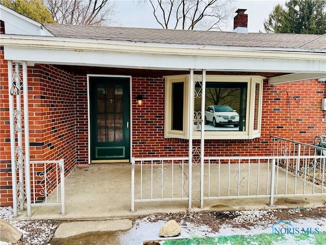 property entrance with a shingled roof, brick siding, and a chimney