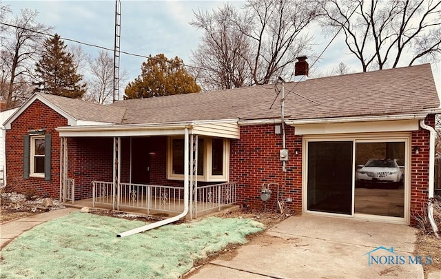 view of front of property with roof with shingles, a chimney, a porch, and brick siding