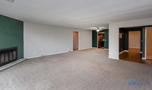 unfurnished living room featuring ceiling fan, dark carpet, and a textured ceiling