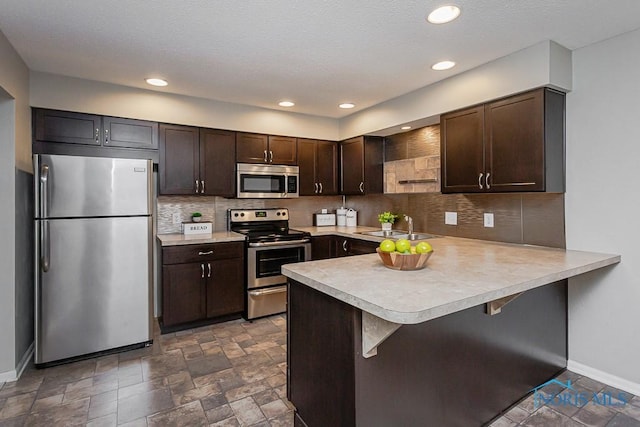 kitchen featuring sink, a breakfast bar area, dark brown cabinets, stainless steel appliances, and kitchen peninsula