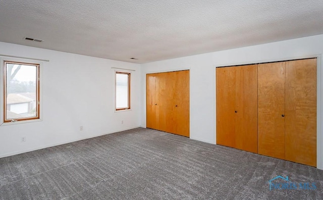 unfurnished bedroom featuring two closets, a textured ceiling, and dark colored carpet