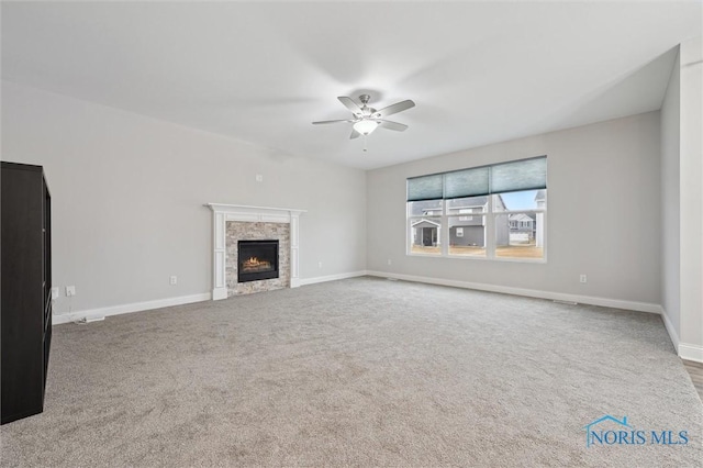 unfurnished living room with a stone fireplace, carpet flooring, and ceiling fan