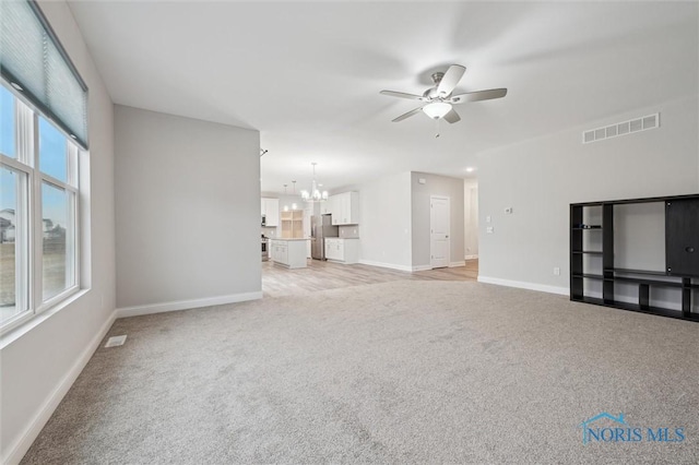 unfurnished living room with ceiling fan with notable chandelier and light colored carpet