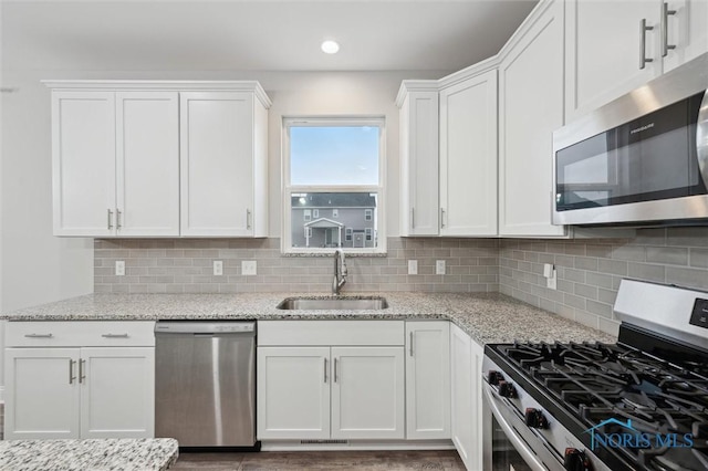 kitchen with sink, stainless steel appliances, light stone counters, white cabinets, and decorative backsplash