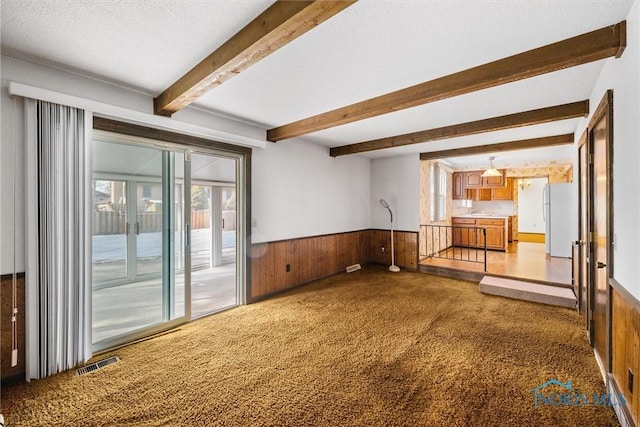 unfurnished room featuring beamed ceiling, a textured ceiling, and wooden walls