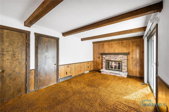 unfurnished living room with wooden walls, a fireplace, carpet flooring, a textured ceiling, and beam ceiling