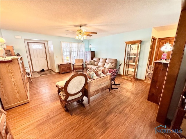 living room featuring light hardwood / wood-style flooring, ceiling fan, and a textured ceiling