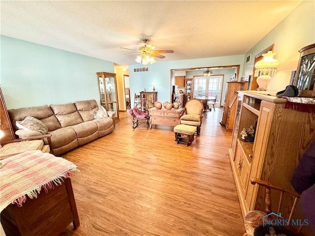 living room featuring light wood-type flooring, ceiling fan, and a textured ceiling